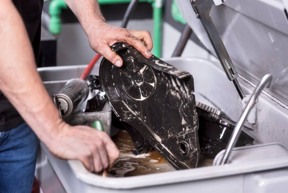 Mechanic degreasing a car engine part at service repair station